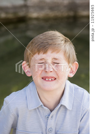 A boy in a blue shirt, screwing his nose up with his eyes tight shut. 11925665
