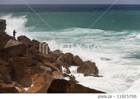 A fisherman standing on the rocks surf casting in the white waves on the Antlantic coast. 11925700