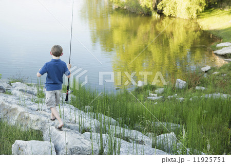 A boy with his fishing rod on the shore of a lake or river.  11925751