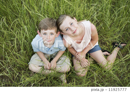 Brother and sister sitting side by side, in long grass.  11925777