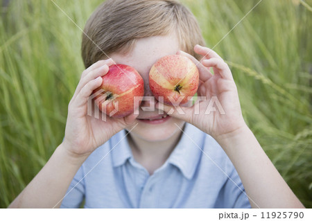 A boy holding two red skinned apples over his eyes.  11925790