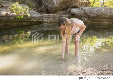 A young girl leaning down to put her hand in shallow water. A young girl leaning down to put her hand in shallow water. 11925822