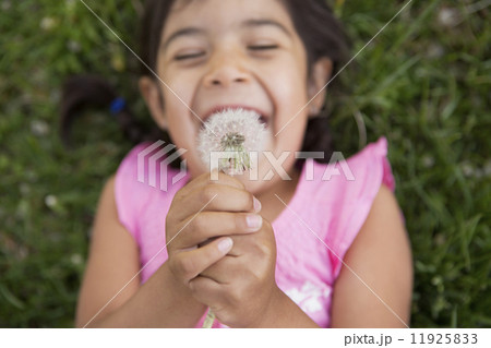 A girl lying on the ground, holding a dandelion seedhead clock. 11925833
