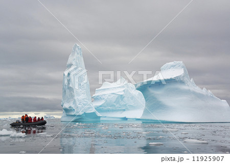 People in small inflatible zodiac rib boats passing towering sculpted icebergs on the calm water around small islands of the Antarctic Peninsula. 11925907