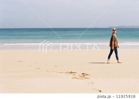 A woman walking barefoot on a beach, leaving footprints in the sand. 11925916