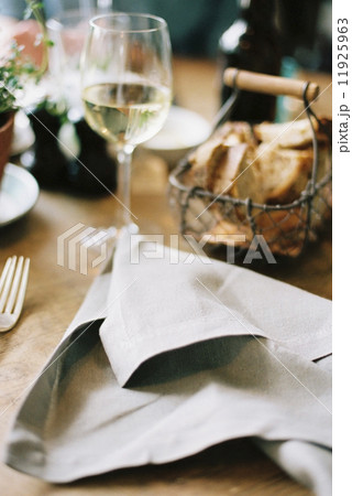 A meal laid out on a table, bread in a basket, wine in a glass and a discarded napkin. 11925963