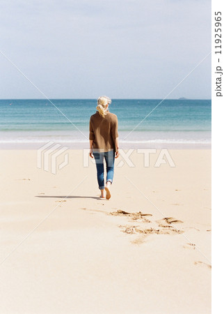 A woman walking barefoot on a beach, leaving footprints in the sand. 11925965