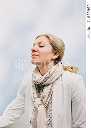 A woman with blonde hair sitting with her eyes closed and her head tilted back, feeling the sun on her face. 11925969
