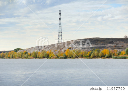High voltage line and electricity pylon on coastline of river. 11957790