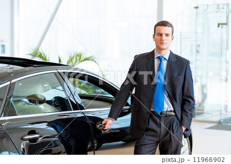 dealer stands near a new car in the showroom 11966902