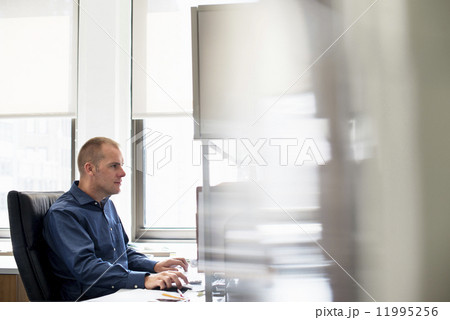 A man working in an office at a desk using a computer mouse. Focusing on a task. 11995256