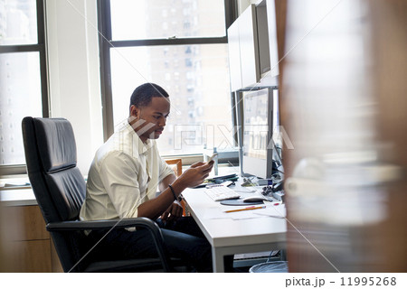 A man sitting in an office, checking his smart phone. 11995268