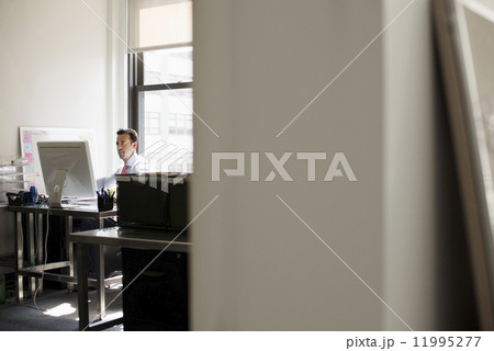 A man seated at a desk in an office, using a computer. A man seated at a desk in an office, using a computer. 11995277