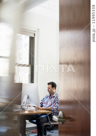 A man working in an office at a desk using a computer. 11995338