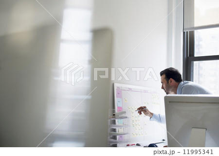 A man using a pen to mark a wall chart or project plan on an office wall. 11995341