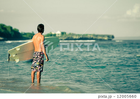 surfer with surfboard walks along the beach in the day time 12005660