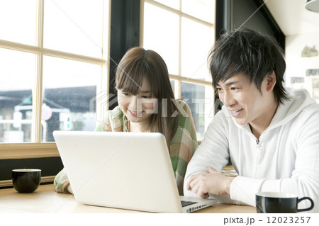 カフェでノートパソコンを見る若いカップル カフェでノートパソコンを見る若いカップル 12023257
