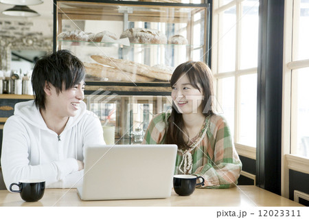 カフェでノートパソコンを見る若いカップル 12023311