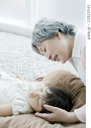 お昼寝中の孫娘を見るシニア女性 お昼寝中の孫娘を見るシニア女性 12023541