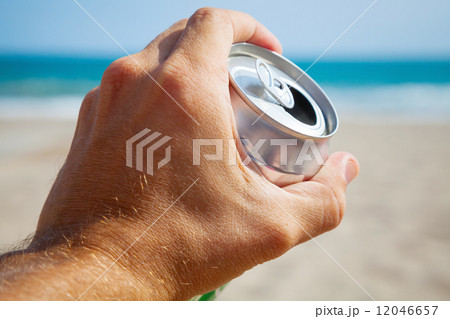 Aluminum can of beer in a male hand with beach and sea on backgr Aluminum can of beer in a male hand with beach and sea on backgr 12046657