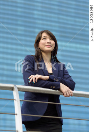 Young successful Chinese business woman standing along reling looking away in front of building Young successful Chinese business woman standing along reling looking away in front of building 12058994