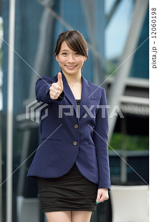 One young successful Chinese business woman giving one thumbs up in front of glass office building One young successful Chinese business woman giving one thumbs up in front of glass office building 12060198