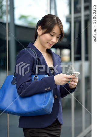 One young successful Chinese business woman using smart phone in front of glass door 12060225