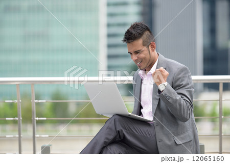 One successful young Malay business man using laptop along promenade in front of office building  12065160