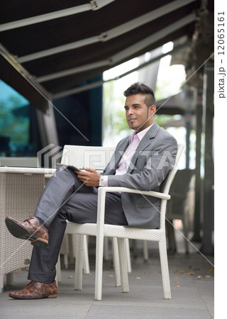 One successful young Malay business man using mobile device tablet iPad at outdoor cafe 12065161