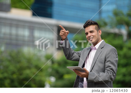 One successful Malay business man along promenade with tablet iPad pointing at his next development One successful Malay business man along promenade with tablet iPad pointing at his next development 12065430