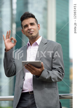 One successful Malay business man with tablet iPad showing OK in front of office building One successful Malay business man with tablet iPad showing OK in front of office building 12065451