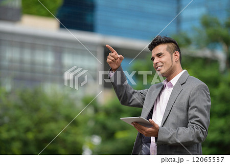 One successful Malay business man along promenade with tablet iPad pointing at his next development One successful Malay business man along promenade with tablet iPad pointing at his next development 12065537