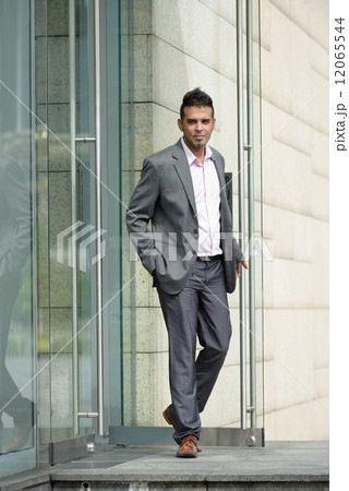One successful young Malay business man walking out of glass door office building 12065544