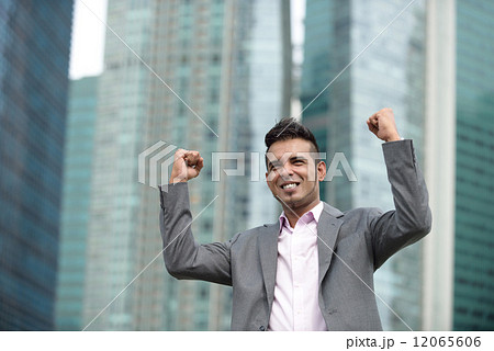 Victorious young successful Malay business man punching fist in the air in front of office buildings Victorious young successful Malay business man punching fist in the air in front of office buildings 12065606