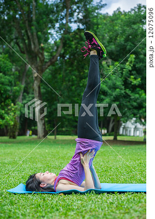 A young and beautiful Asian lady is performing yoga on a yoga mat in the garden / park 12075096