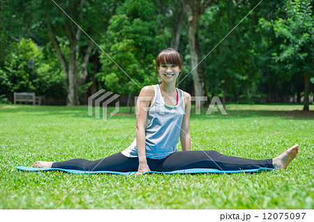 A smiling young and beautiful Asian lady doing yoga on a yoga mat in the garden 12075097