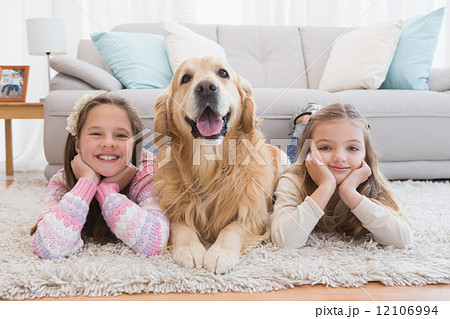 Sisters lying on rug with golden retriever smiling at camera 12106994