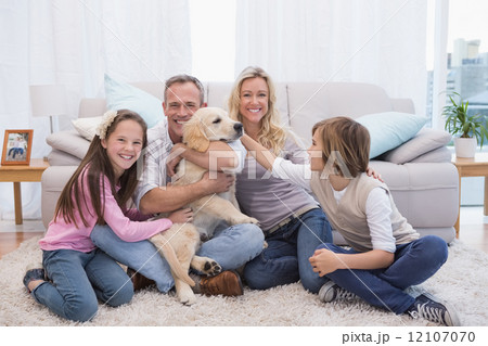 Smiling family with their pet yellow labrador on the rug 12107070