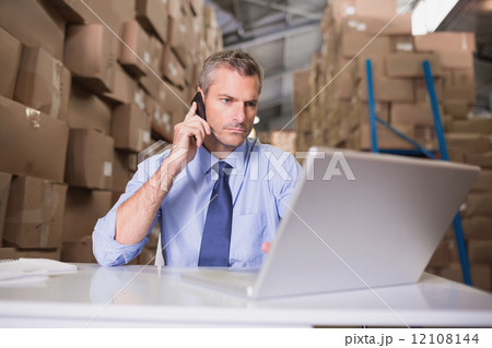 Warehouse manager using cellphone and laptop Warehouse manager using cellphone and laptop 12108144