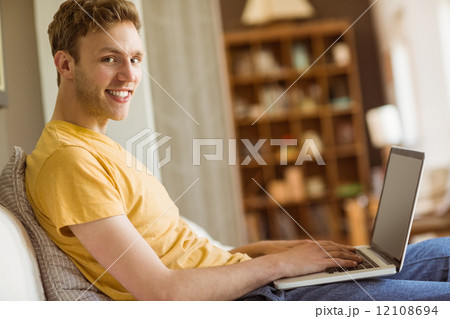 Young man using laptop on his couch Young man using laptop on his couch 12108694