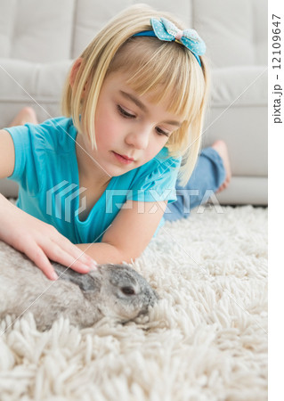 Little girl lying on rug stroking the rabbit 12109647