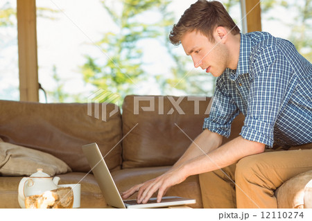 Young man using laptop on his couch Young man using laptop on his couch 12110274