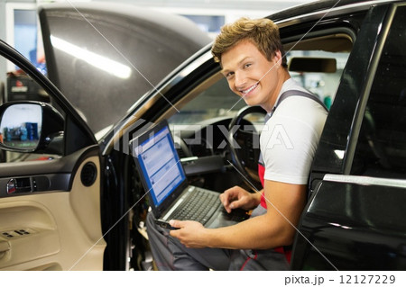 Serviceman making car diagnostics with laptop in a workshop 12127229