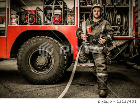 Firefighter near truck with equipment with water water hose over shoulder Firefighter near truck with equipment with water water hose over shoulder 12127401