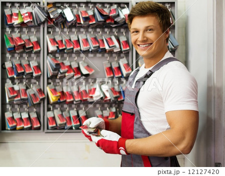 Cheerful serviceman near stand with colour samples in car body workshop Cheerful serviceman near stand with colour samples in car body workshop 12127420