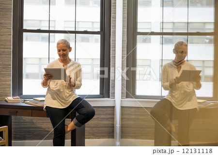 Office life.A woman seated on the edge of her desk using a digital tablet. Office life.A woman seated on the edge of her desk using a digital tablet. 12131118