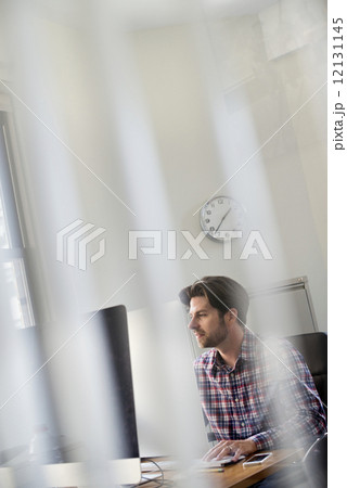 View through an office partition of a man seated at a desk. View through an office partition of a man seated at a desk. 12131145
