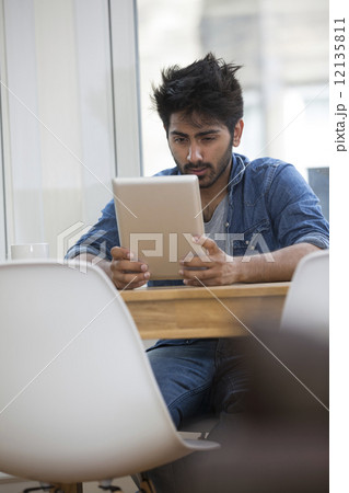 Asian man sitting at a table reading a Tablet PC. 12135811