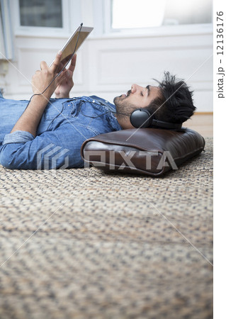 Indian lying on floor at home reading a Tablet PC. 12136176