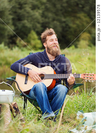 smiling man with guitar and dixie in camping 12139578